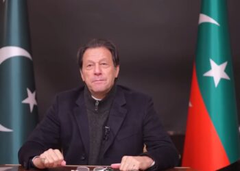 Former Pakistani Prime Minister Imran Khan sits between the Pakistani and PTI flags